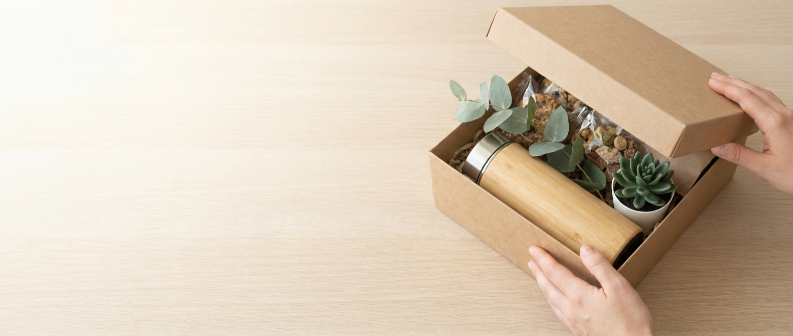 An open sustainable corporate gift box with recycled packaging, a plant and eco treats on a sunlit desk